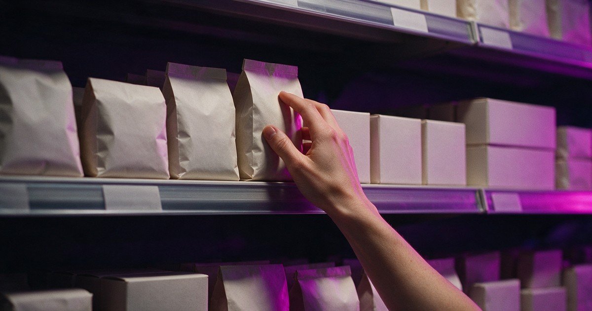 Mão alcança uma embalagem de papel sem rótulo em uma prateleira de loja.